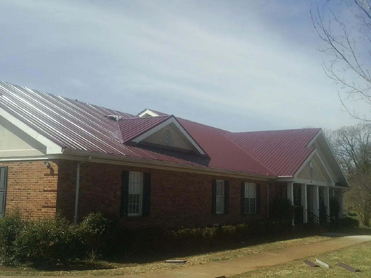 Red metal roof with gabled entries on a long brick building, from a Hail Damage Roof Repair job in Manor