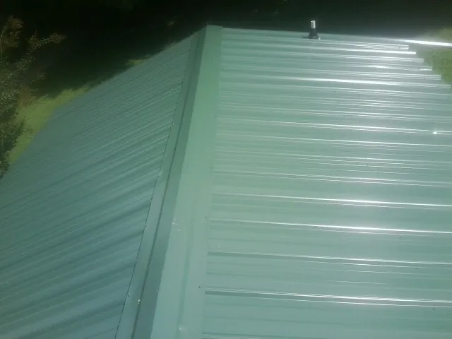 New green metal panels meeting at the ridge of a roof — Flat Roof Repair work by our crew in Manor